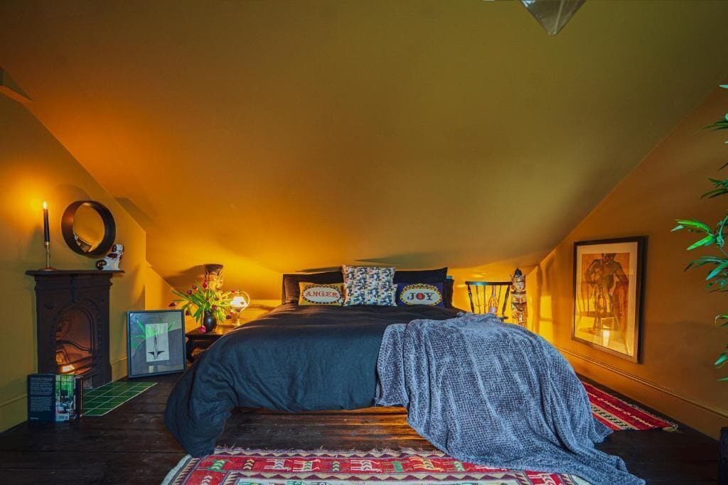 A cozy attic bedroom with a bed, a fireplace, and a large window.