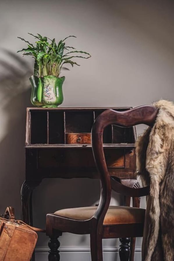 Una silla antigua con asiento acolchado, un jarrón verde con plantas y un bolso de cuero marrón en el suelo.