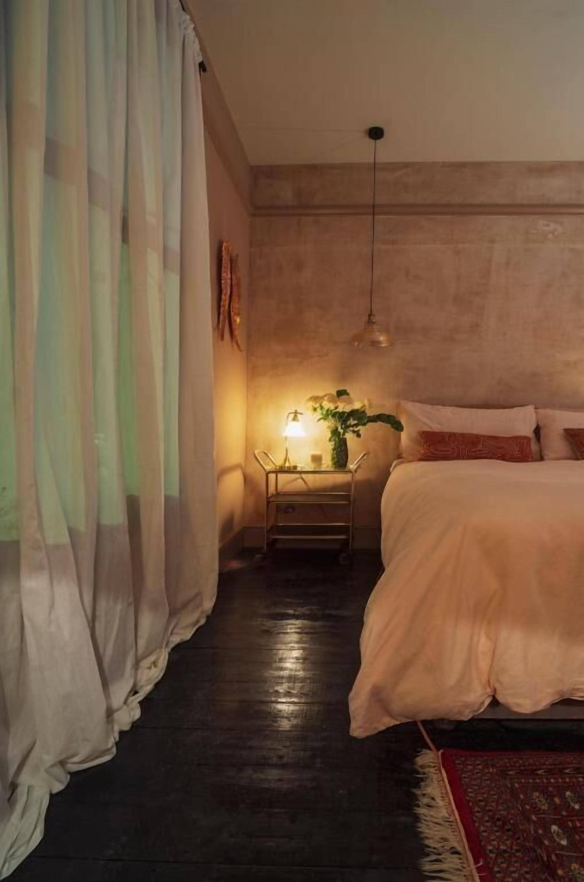 Ein Schlafzimmer mit einem Bett, einem Nachttisch, einer Lampe und einer Pflanze.