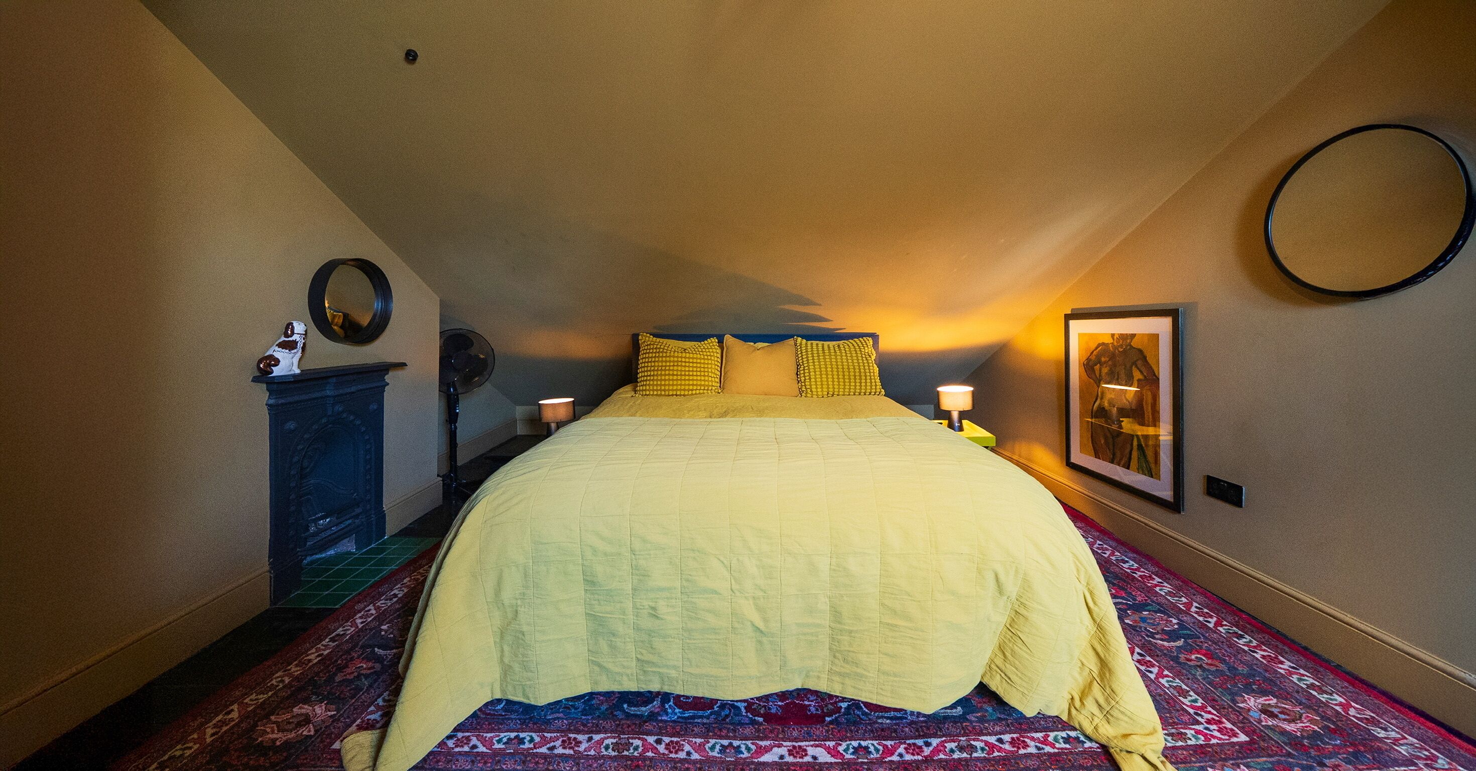 Ein Schlafzimmer mit einem Bett, einem Nachttisch, einer Lampe, einem Spiegel und einem gerahmten Bild an der Wand.