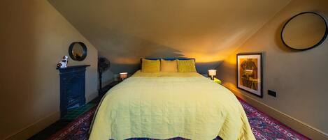 Ein Schlafzimmer mit einem Bett, einem Nachttisch, einer Lampe, einem Spiegel und einem gerahmten Bild an der Wand.