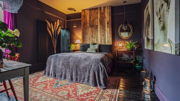 Un dormitorio con cama, un cabecero de madera, una lámpara colgante y un espejo.