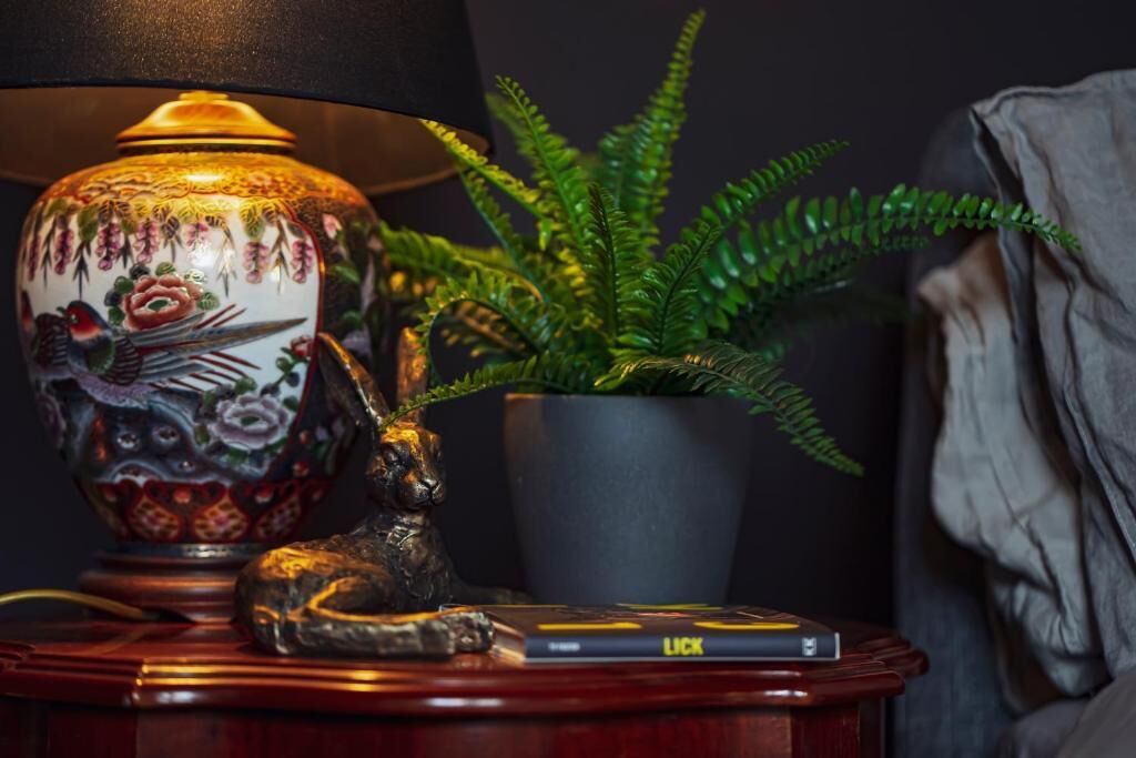 Una lámpara, una planta en maceta, un libro y una estatua sobre una mesa de madera.
