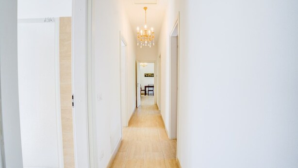 Un pasillo con candelabro, paredes blancas y suelo de madera.