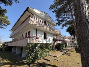 Ein zweistöckiges Gebäude mit Balkon, umgeben von Bäumen und einer Rasenfläche.