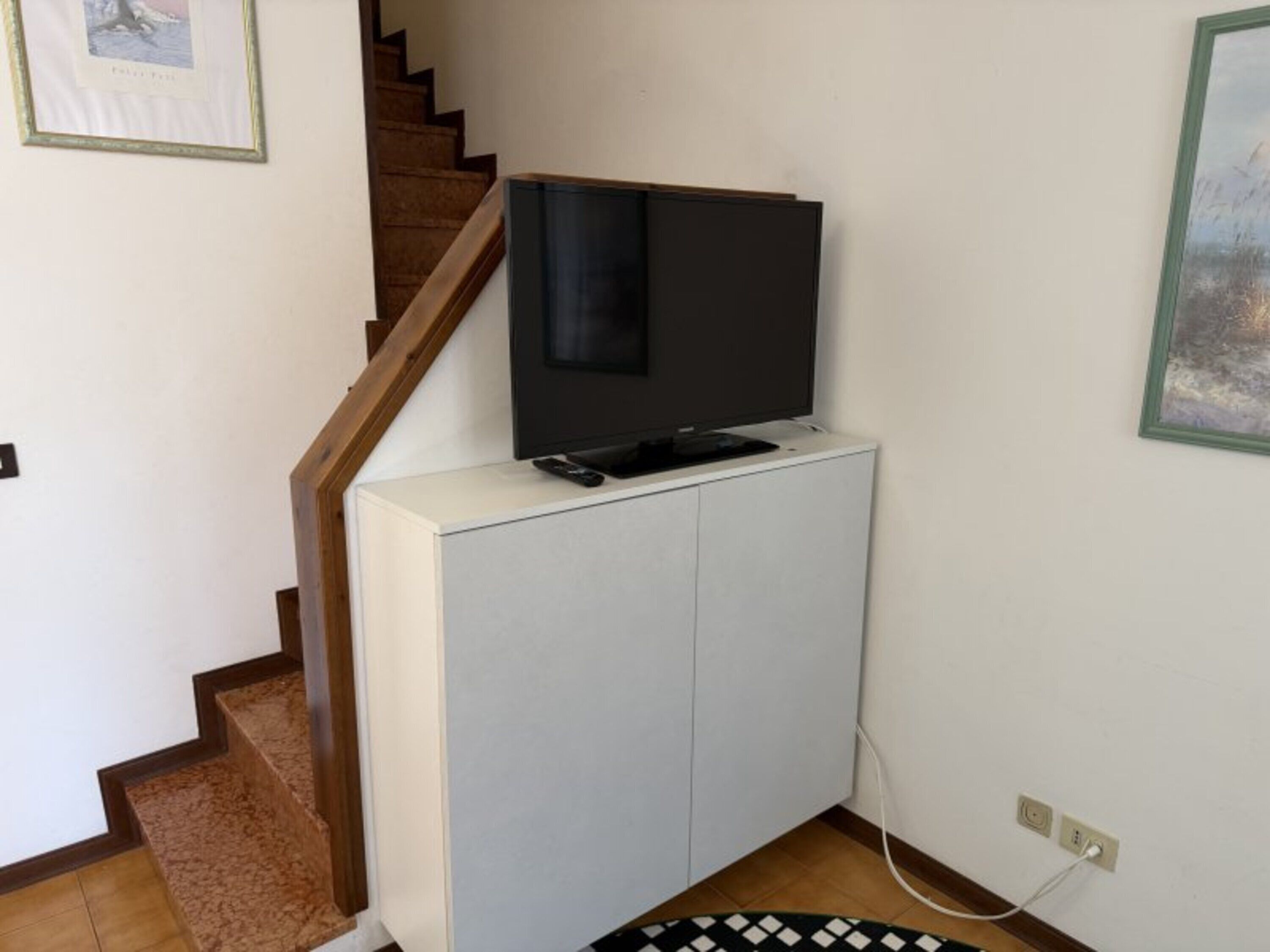 Ein Flachbildfernseher auf einem weißen Schrank, eine Treppe und eine Steckdose an der Wand.