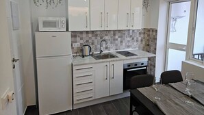 A compact kitchen with white cabinets, a microwave, a kettle, and a sink. There is a dining table with chairs and wine glasses. - 2BR Family Flat * Balcony * Walk to Everything (Málaga)