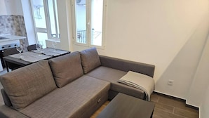 A modern living room with a sectional sofa, a small table, and a view of the balcony. - 2BR Family Flat * Balcony * Walk to Everything (Málaga)