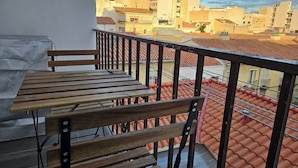 A balcony with a wooden bench and table, overlooking a cityscape with terracotta-tiled roofs. - 2BR Family Flat * Balcony * Walk to Everything (Málaga)