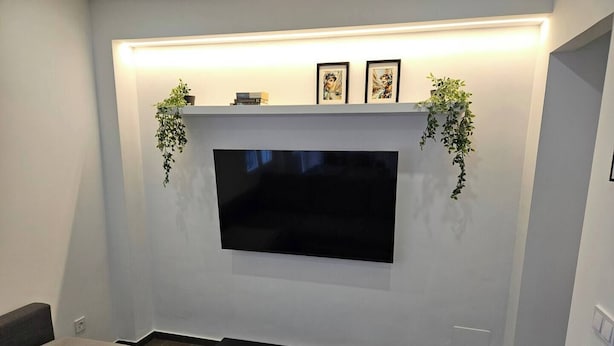 A modern living room with a flat-screen TV mounted on a white wall, a dark wooden coffee table, and a grey sofa. - 2BR Family Flat * Balcony * Walk to Everything (Málaga)