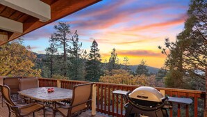 A wooden deck with a table and chairs, a grill, and a view of trees and a sunset. - Hot Tub, Near Bear Mt, Lake Views, Dog Yard, AC (Big Bear Lake)
