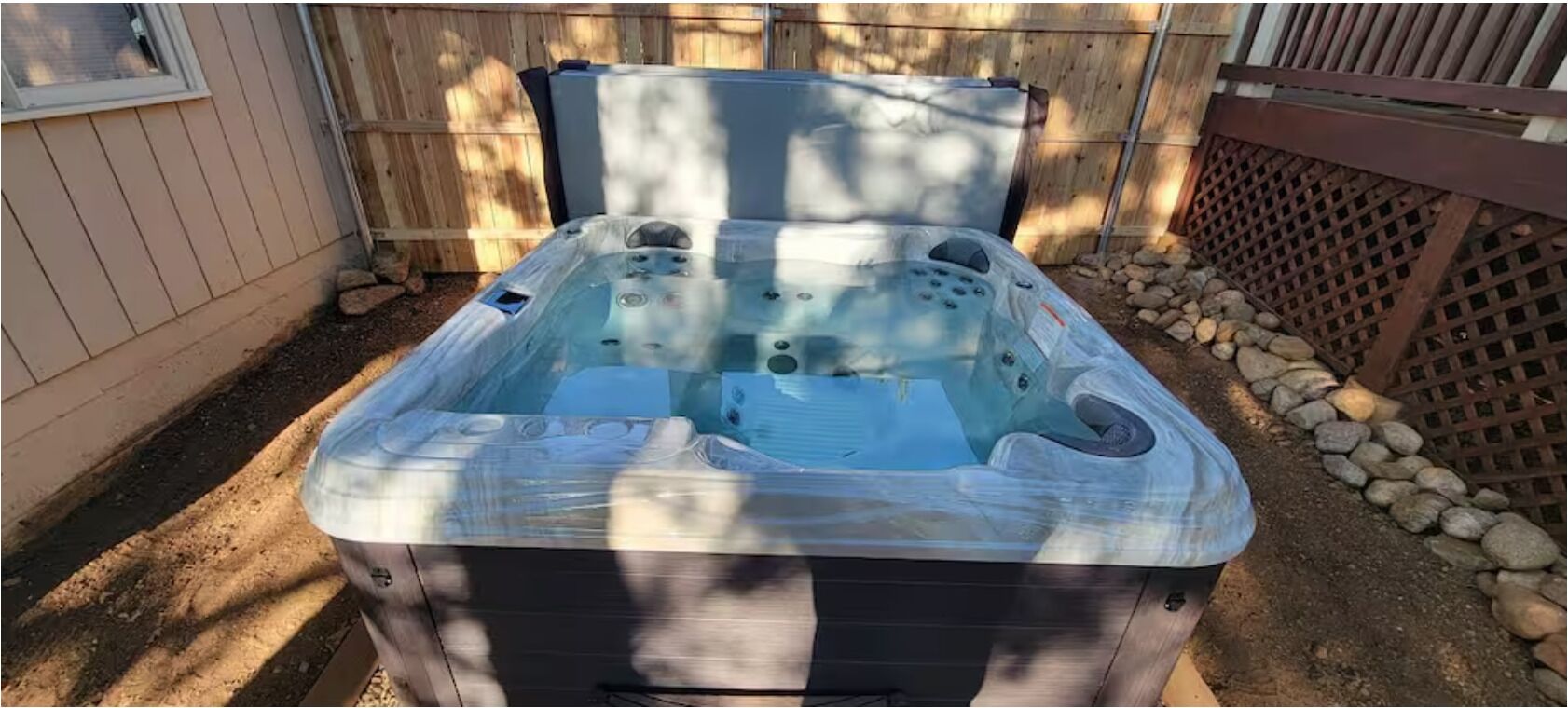 A hot tub with a cover, surrounded by a wooden fence and a stone wall.