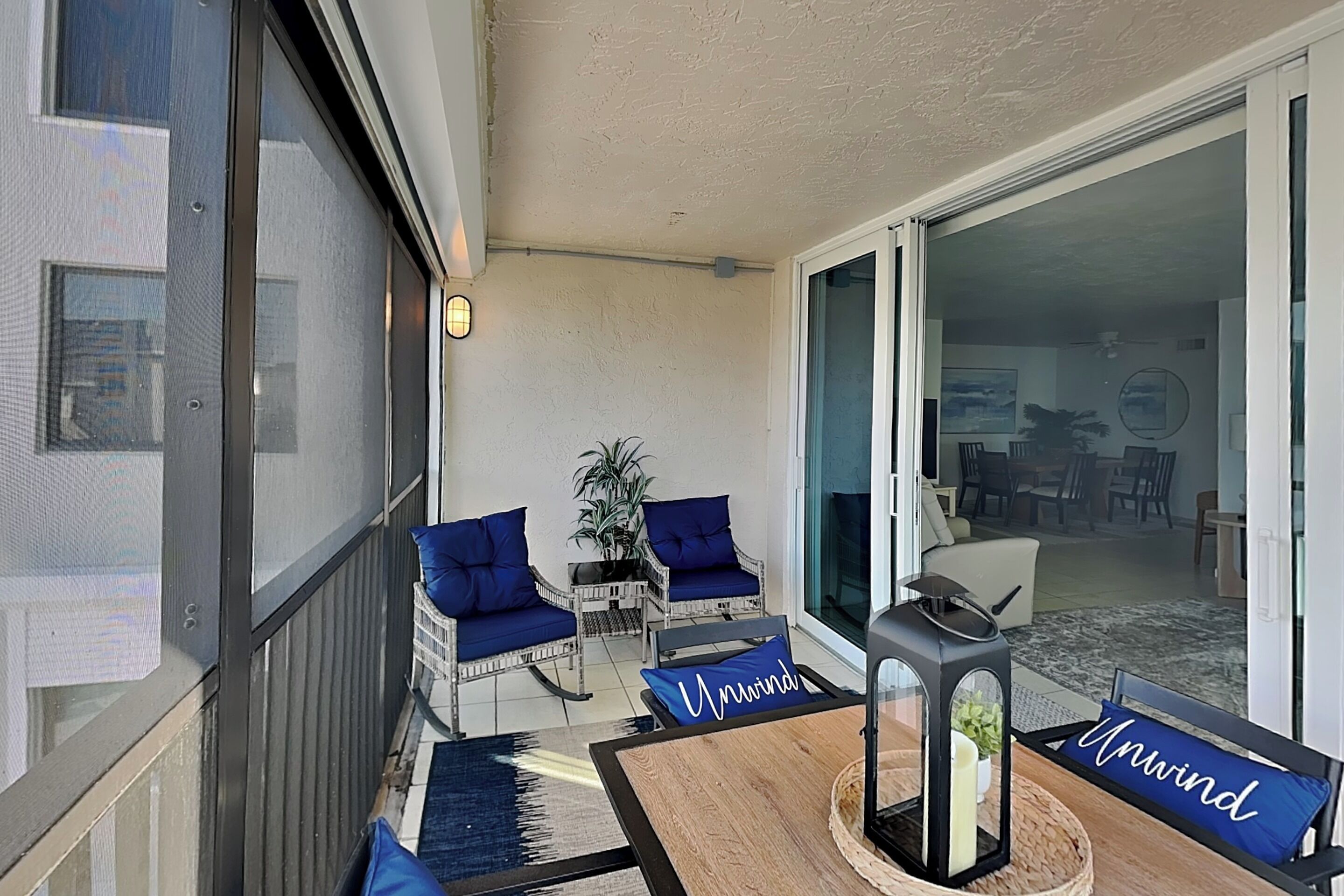 A balcony with two blue cushioned chairs, a small table, and a potted plant.