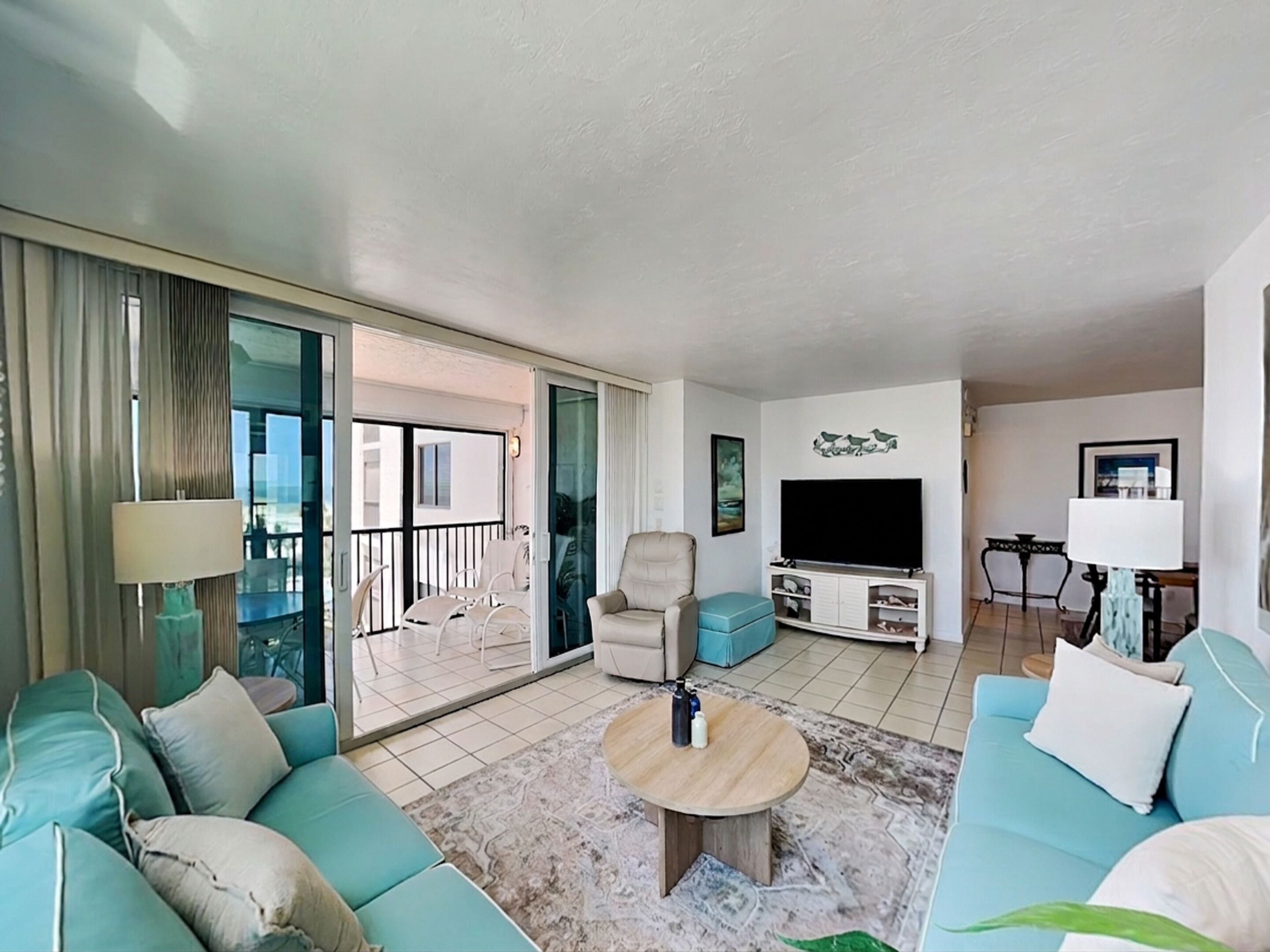 A living room with a sofa, a coffee table, a TV, and a balcony with outdoor furniture.