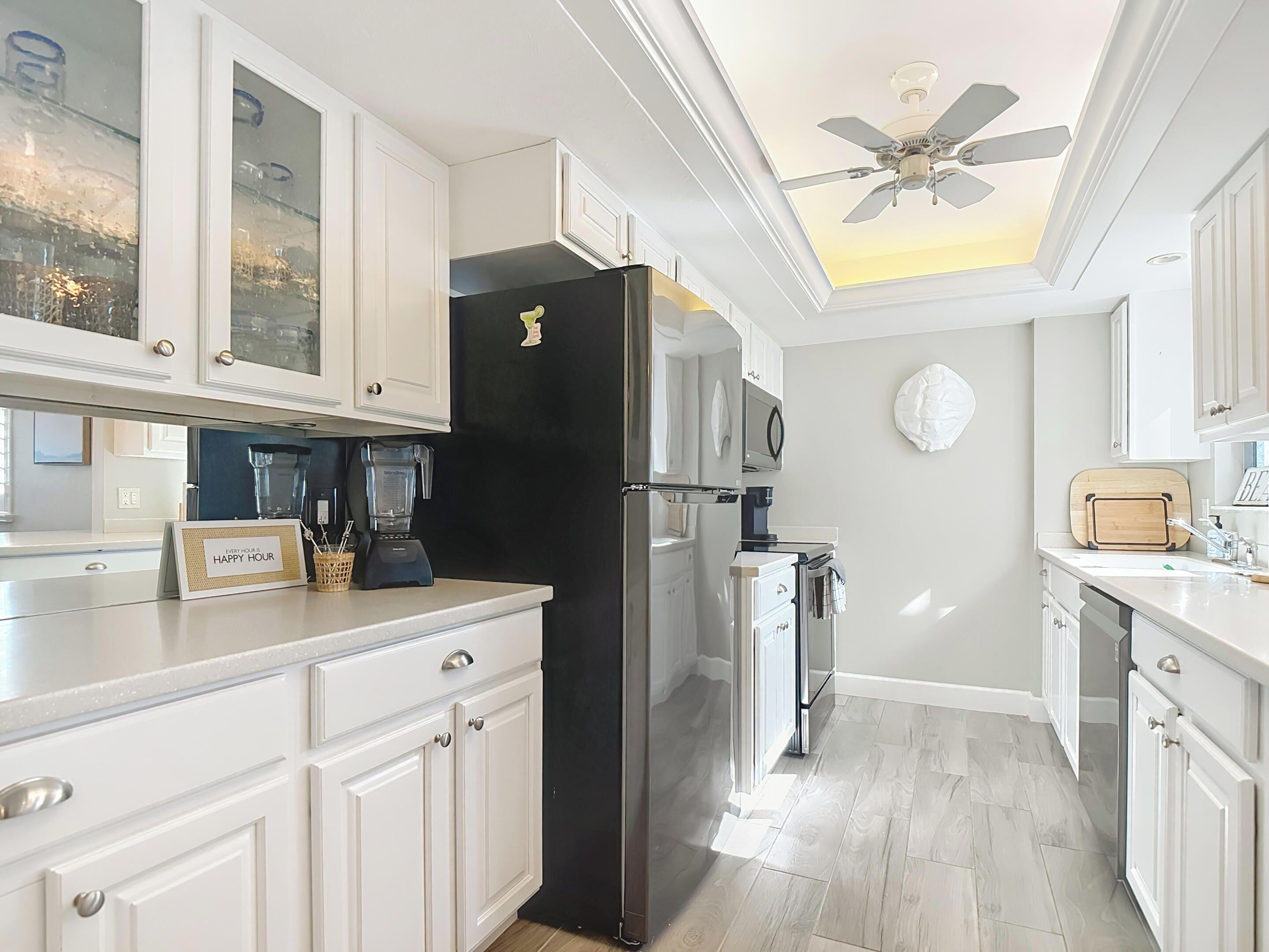 A modern kitchen with white cabinetry, a black refrigerator, a ceiling fan, and a coffee maker.