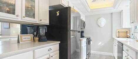 A modern kitchen with white cabinetry, a black refrigerator, a ceiling fan, and a coffee maker.