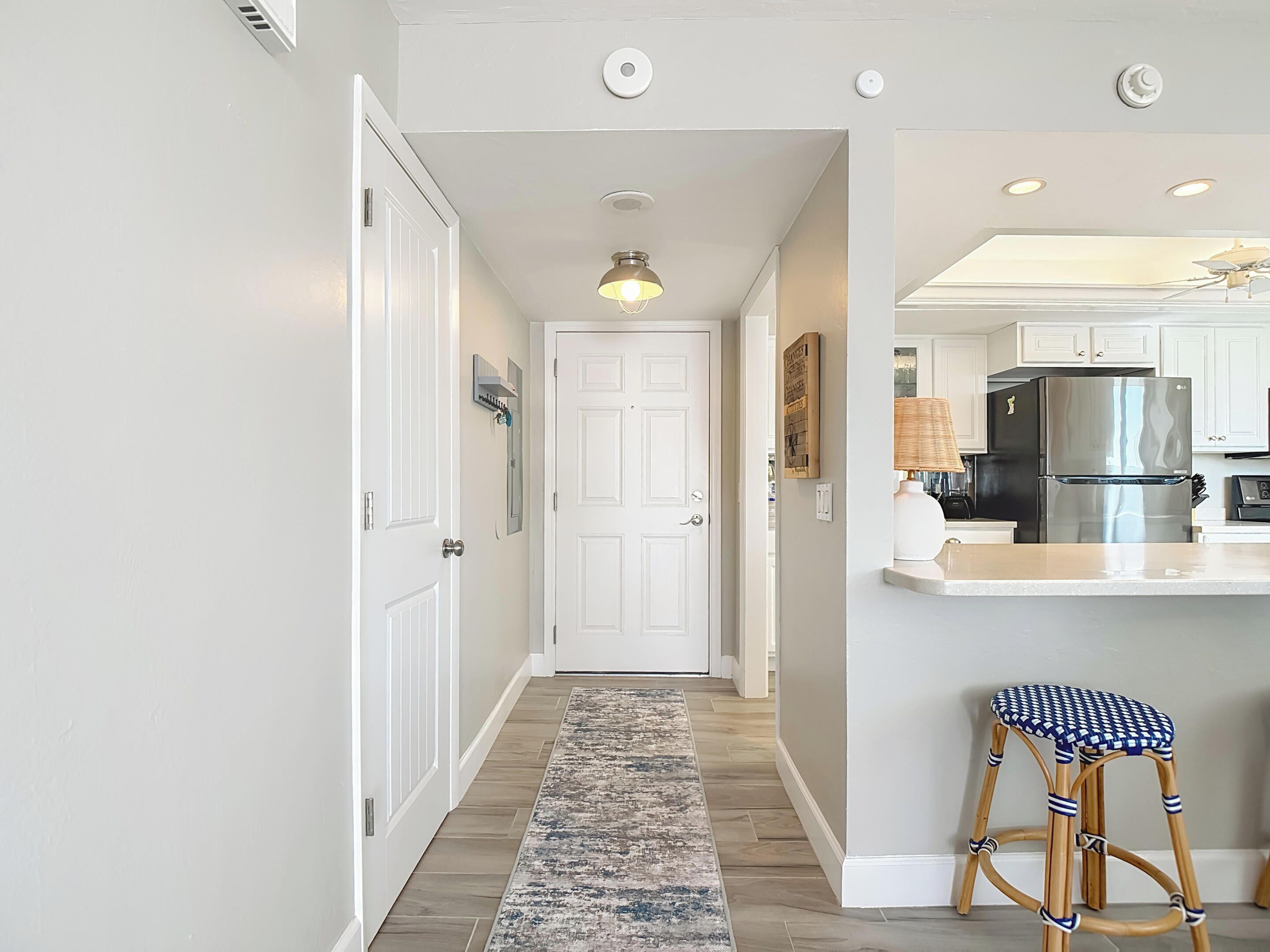 A hallway leading to a kitchen with a refrigerator, a bar stool, and a ceiling fan.