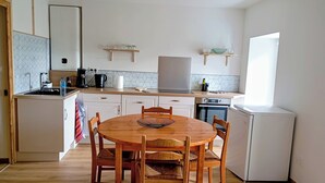A compact kitchen with a round wooden table, white cabinets, and a small refrigerator. - Country apartment close to the Dolce Via and hiking trails (Saint-Agrève)