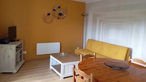 A room with a wooden dining table, a yellow sofa, a white radiator, and a decorative wall piece. - Country apartment close to the Dolce Via and hiking trails (Saint-Agrève)