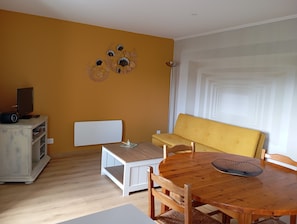 Une pièce comprenant une table à manger en bois, un canapé jaune, un radiateur blanc et un élément décoratif mural.