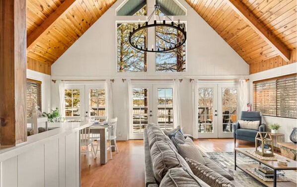 A spacious loft with a high ceiling, a dining area, a large sofa, and a view through the windows. - Lakefront House With AC, Private Dock, Game Loft (Big Bear Lake)