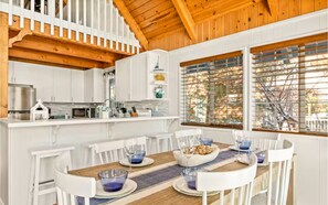 A kitchen with white cabinets, a wooden ceiling, and a dining area with white chairs and blue glassware. - Lakefront House With AC, Private Dock, Game Loft (Big Bear Lake)