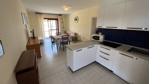 A modern kitchen with white cabinets, a microwave, and a dining area with a table and chairs. - Three-Room Apartment with Solarium, Shared Pool, and Private Terrace (Marina di Bibbona)