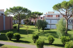 Un quartiere residenziale con un prato curato, diversi alberi e un edificio con tetto piatto e facciata bianca.