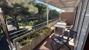 A balcony with a table, chairs, and a view of a landscaped area. - Three-Room Apartment with Solarium, Shared Pool, and Private Terrace (Marina di Bibbona)