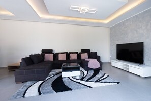 Ein modernes Wohnzimmer mit einem Ecksofa, einem Flachbildfernseher und einem gemusterten Teppich.