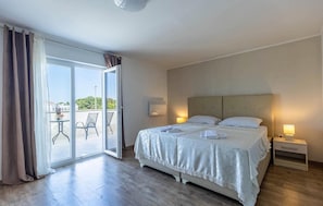 A hotel room with a bed, a nightstand, a lamp, a window with curtains, and a view of the outdoors. - House in city center of Rovinj (Rovinj)