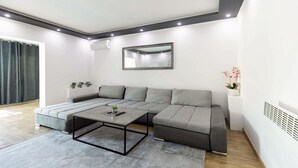 Ein modernes Wohnzimmer mit einer Eckcouch, einem Couchtisch, einem großen Spiegel und einer Topfpflanze.