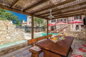 Ein hölzerner Essbereich im Freien mit Pool, Steinmauern und einer überdachten Sitzgruppe.