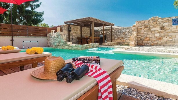 A pool area with a stone wall, a wooden pergola, and lounge chairs with towels. - Holiday house in a peaceful village (Svetvincenat)