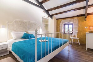 Ein Schlafzimmer mit einem Bettgestell aus weißem Metall, einer blauen Bettdecke, einem weißen Nachttisch, einem weißen Stuhl und einem kleinen Schreibtisch mit Lampe.