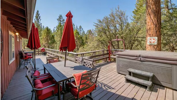 Una terraza de madera con mobiliario exterior, un jacuzzi y un árbol con un letrero.