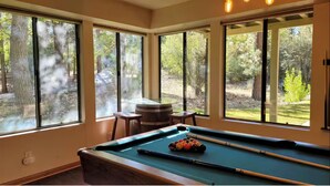 Une table de billard placée devant de grandes fenêtres donnant sur une zone boisée.