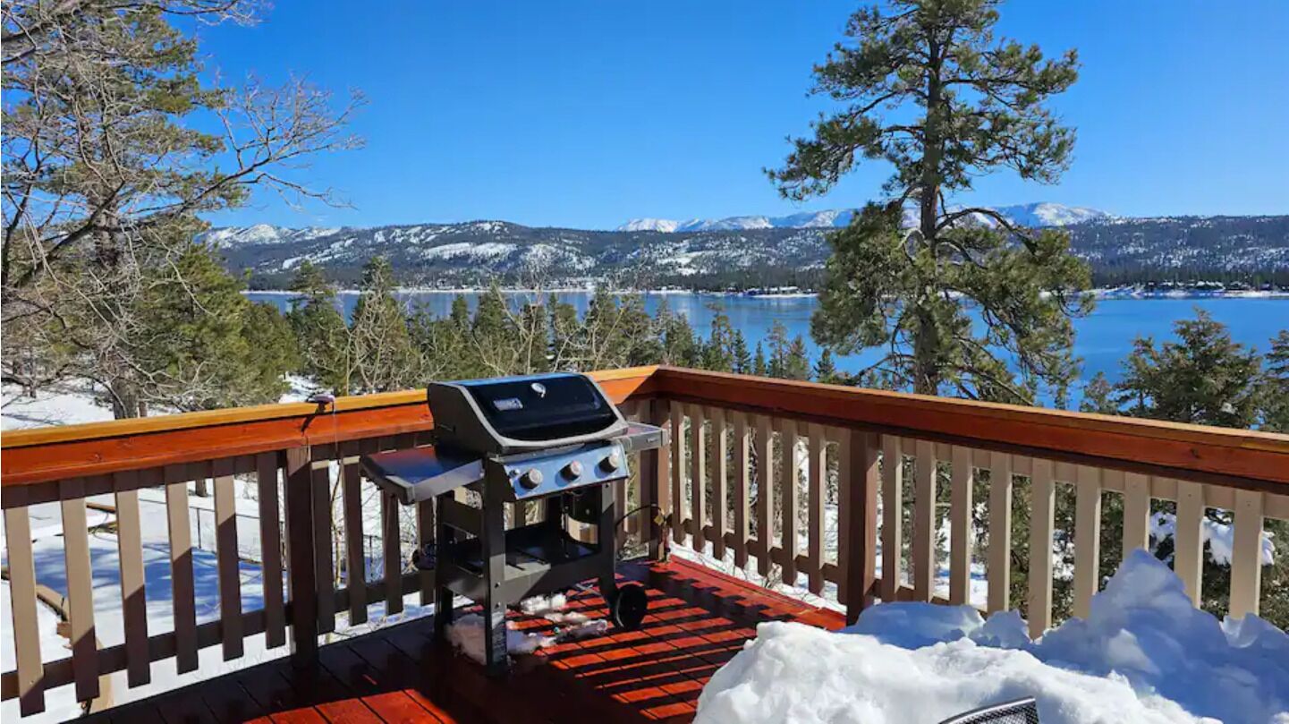 A deck with a barbecue grill overlooking a lake and mountains.