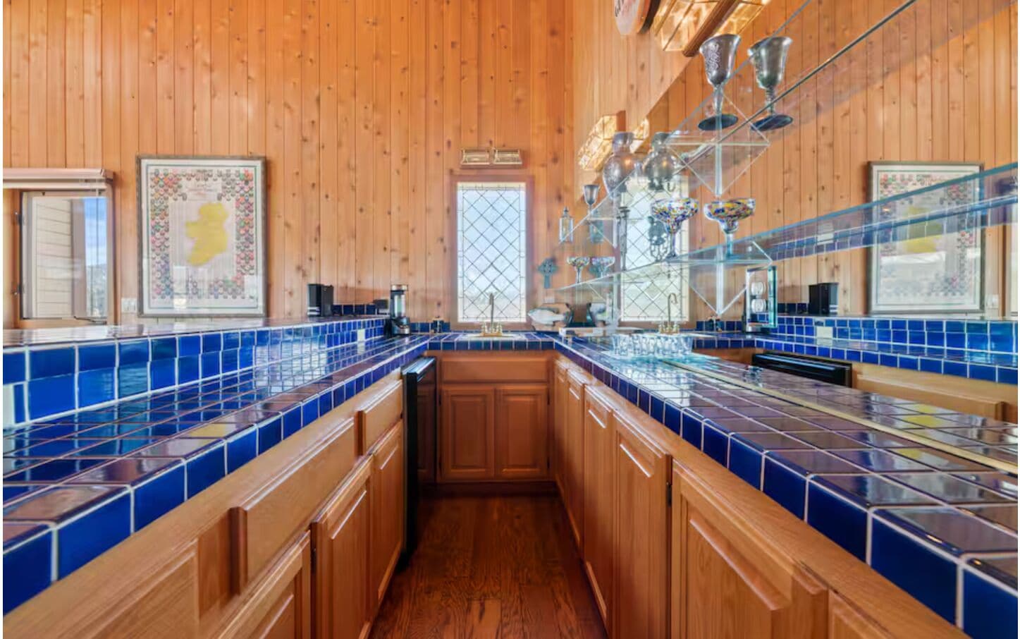 A kitchen with wooden cabinets, blue tiled countertops, and a window with a decorative glass door.