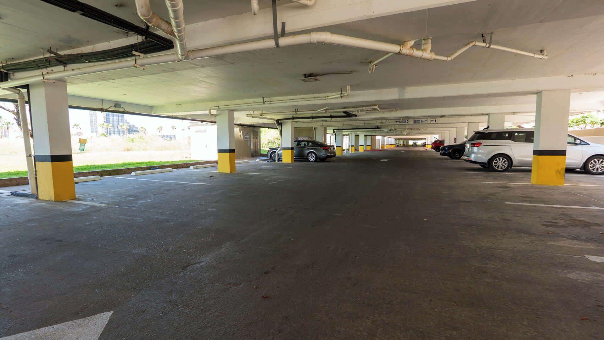 Un parcheggio multipiano con pilastri in cemento e tubature a vista.