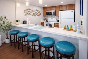 Una cocina con armarios de madera, una encimera blanca y cuatro taburetes azules.