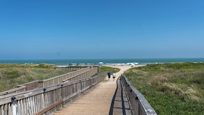 Una pasarela de madera que conduce a una playa con dunas y un cielo azul despejado.