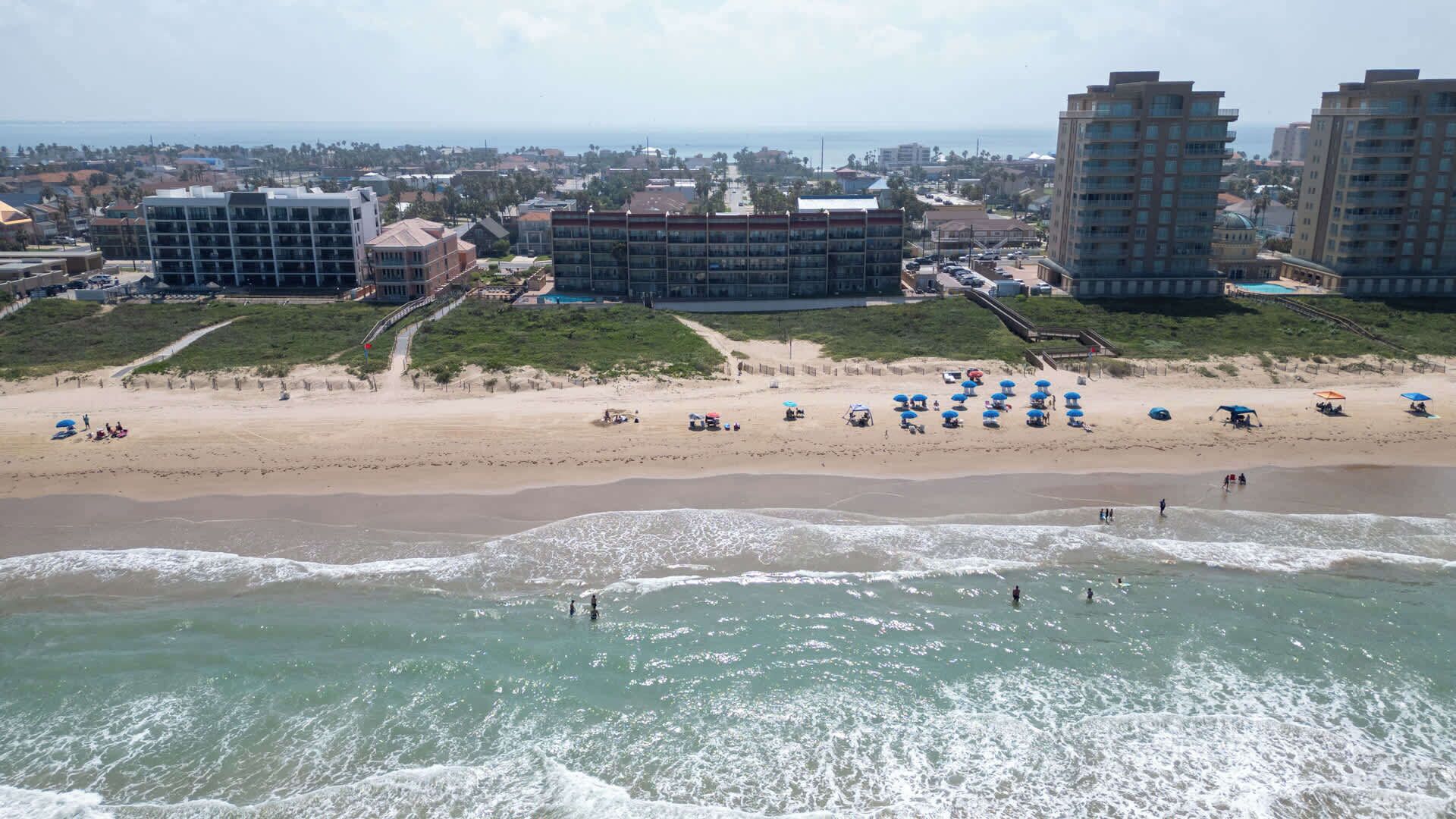 Een strand met parasols en mensen, een promenade en gebouwen op de achtergrond.