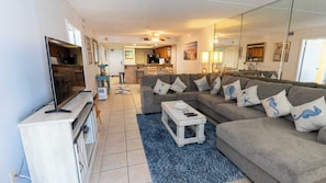 Ein Wohnzimmer mit Sofa, Fernseher und einer Küche im Hintergrund.