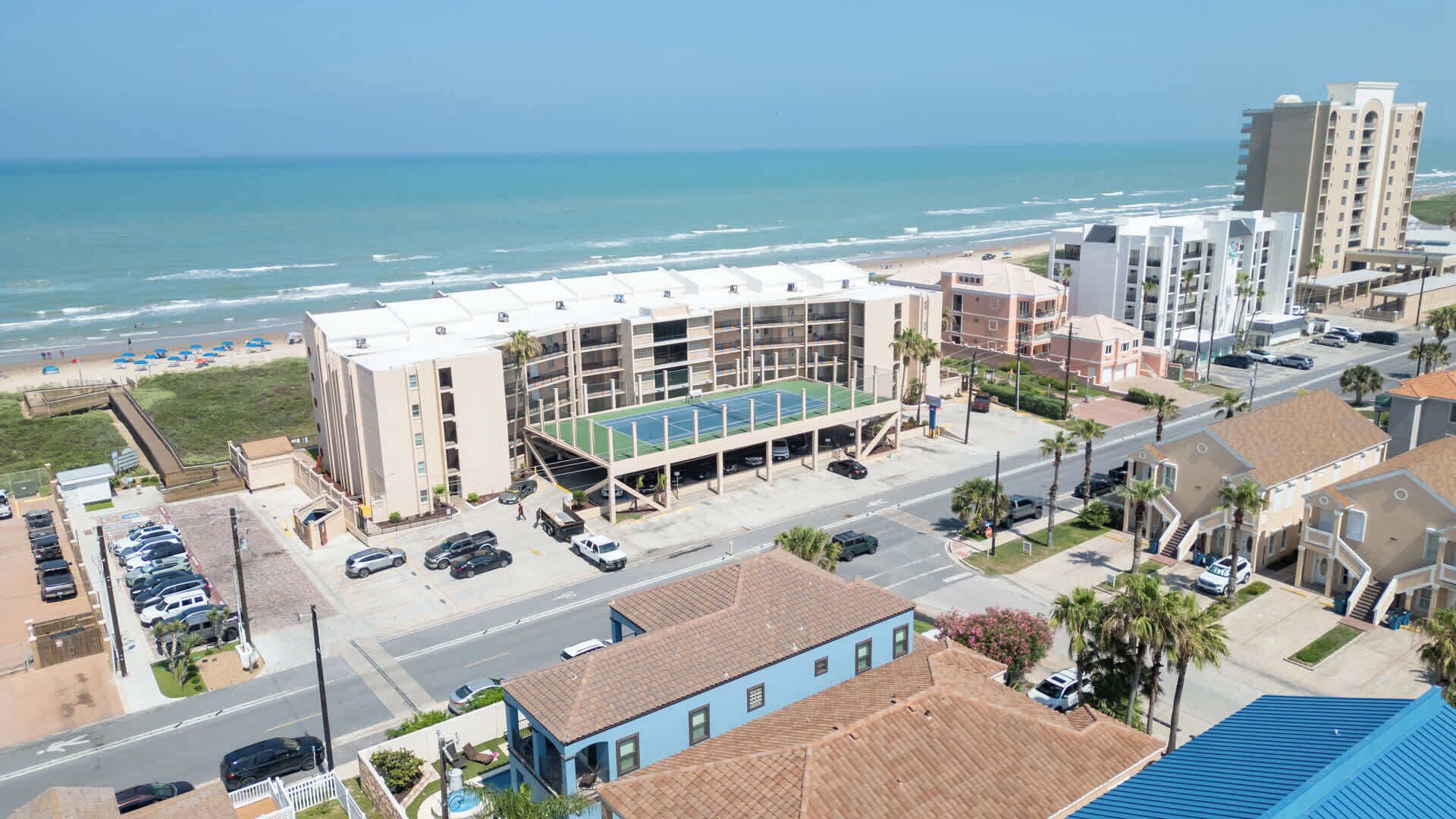 A multi-story hotel with a rooftop tennis court, adjacent to a beach and ocean view.