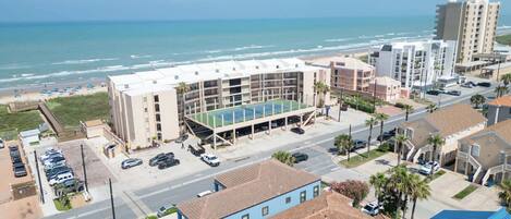 A multi-story hotel with a rooftop tennis court, adjacent to a beach and ocean view.