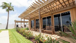 Eine überdachte Terrasse im Freien mit Holzmöbeln, einer Palme und Blick auf den Himmel.