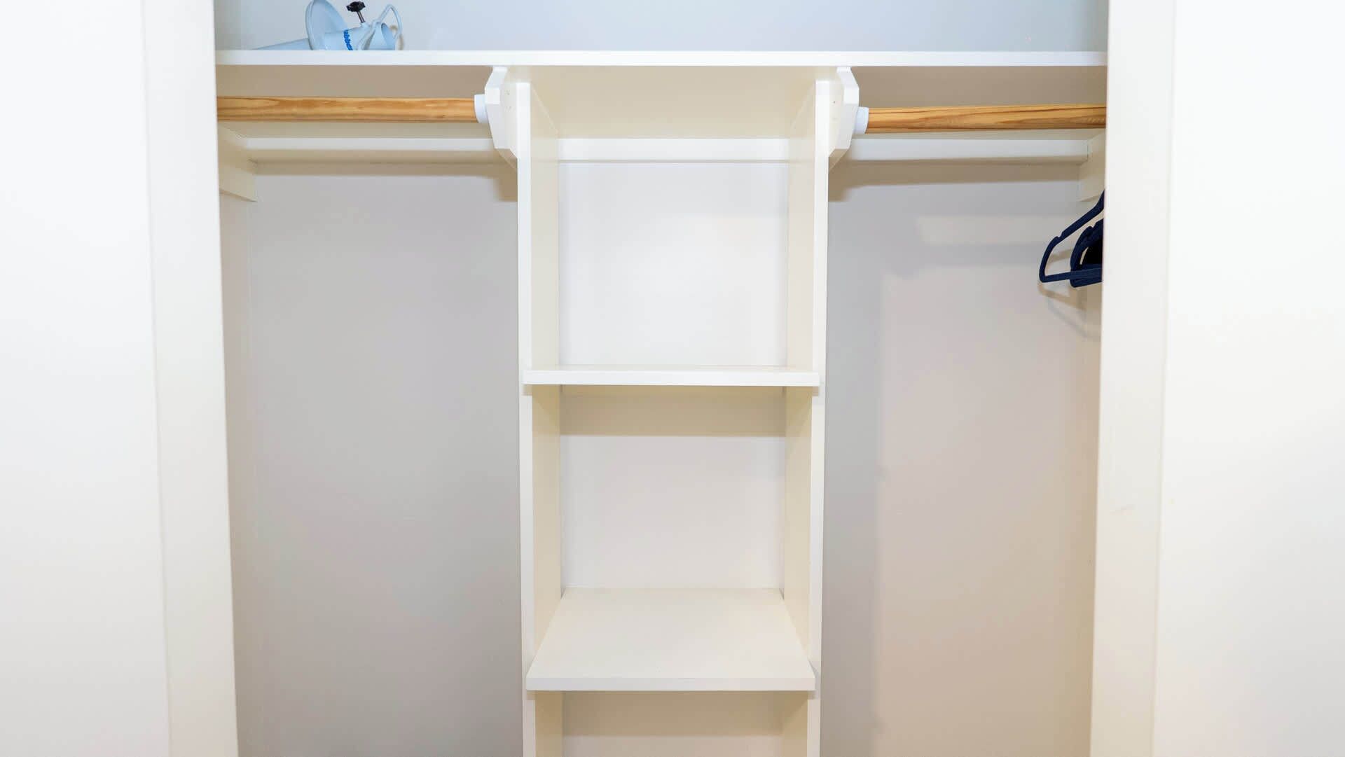 A closet with a wooden rod and two white shelves.