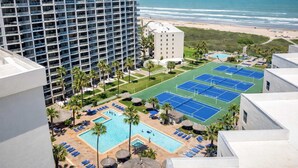 Een hotel met een zwembad op het dak, tennisbanen en uitzicht op het strand.