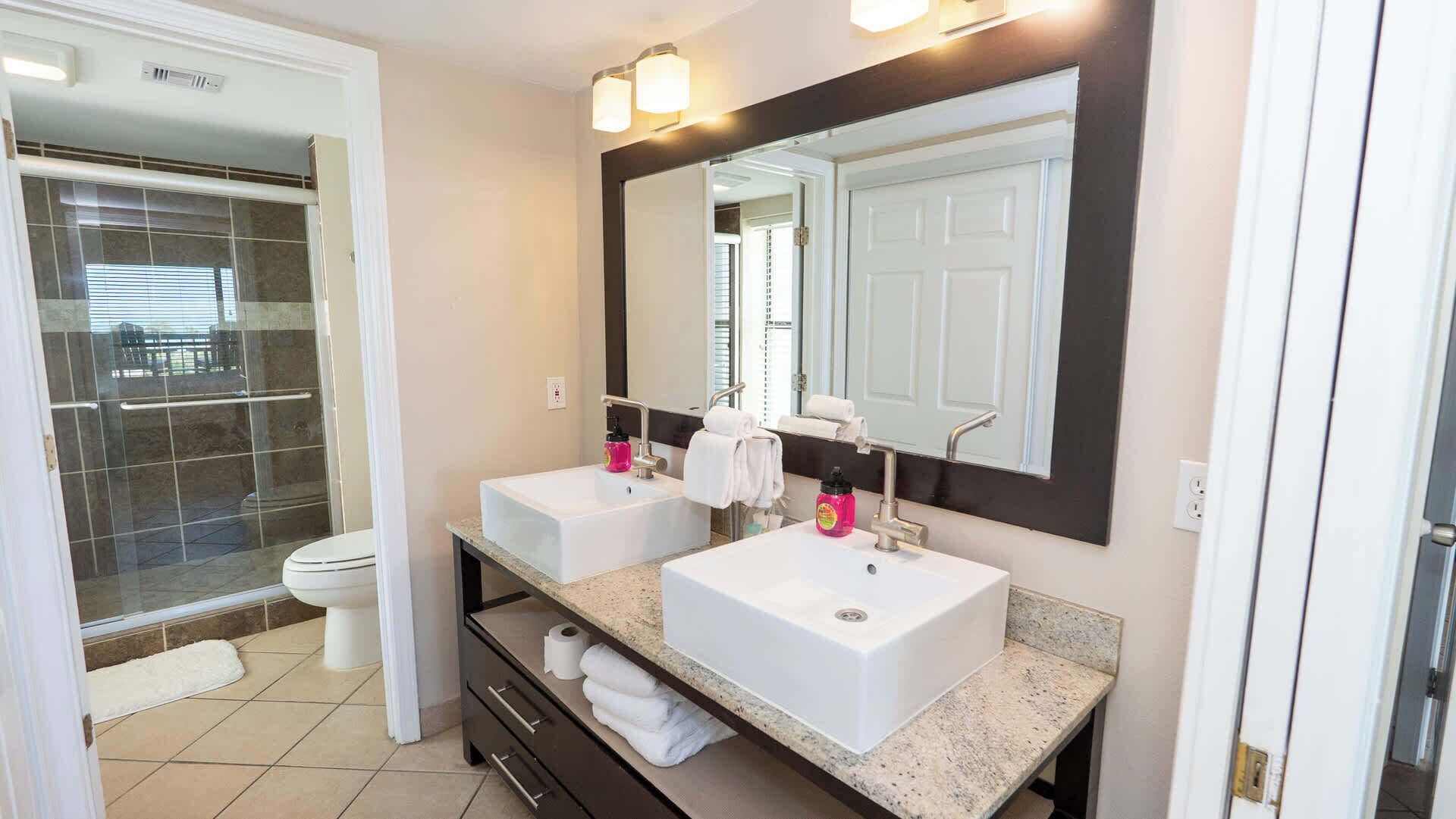 A bathroom with two sinks, a large mirror, and a shower.